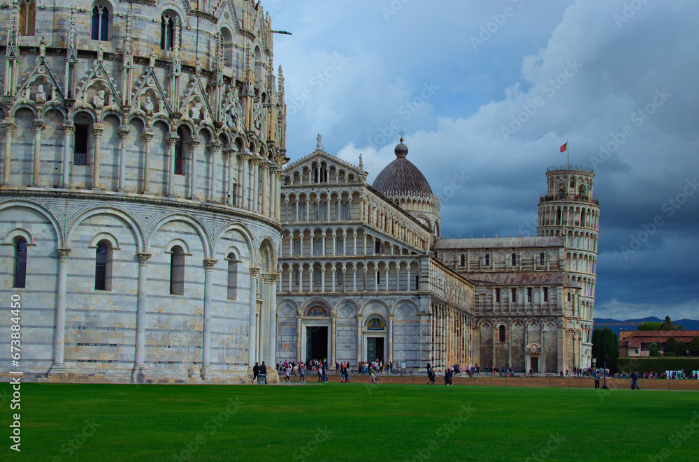 Picturesque landscape view of Pisa Baptistery, Pisa Cathedral and Leaning Tower of Pisa against stormy sky and gloomy clouds. Notable landmark of Pisa, Italy. UNESCO World Heritage Site