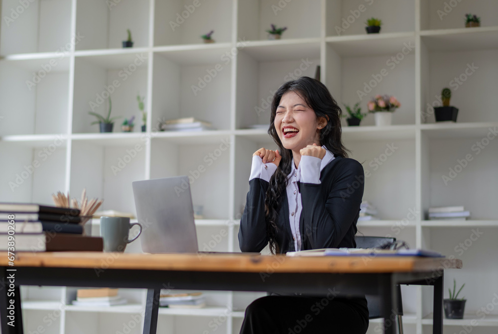 Happy Asian woman celebrates victory while receiving good news while working in modern office. Excited about success. Happy Asian woman celebrates victory while receiving good news while working in modern office. Excited about success.