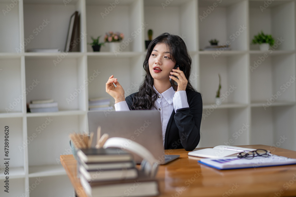 Freelance Asian woman talking on the phone with friend or colleague while working on laptop Freelance Asian woman talking on the phone with friend or colleague while working on laptop