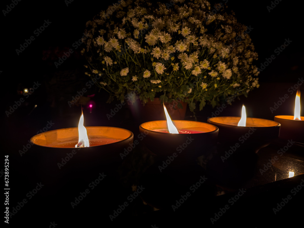trzy ceramiczne znicze płonące na nagrobku stojące obok kwiecistej chryzantemy - obrazy, fototapety, plakaty 
