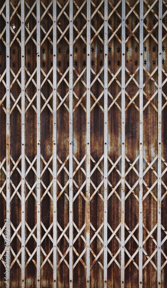 Naklejka premium Rusty steel collapsible door texture, old fashion style shutter gate.Folding old red metal door gate, Rust corrosion in old iron door.Grunge rusted metal texture, oxidized background.Vertical.