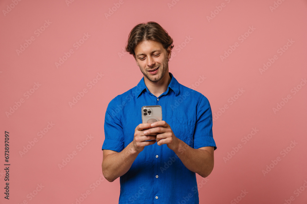 Smiling man using smartphone while standing isolated over pink background Smiling man using smartphone while standing isolated over pink background