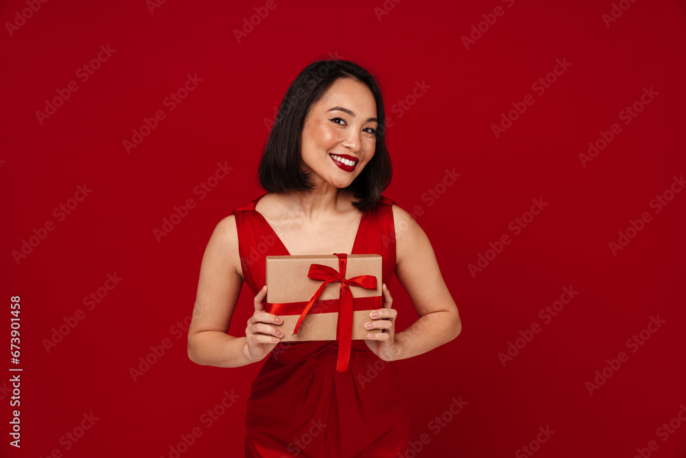 Happy woman holding gift box while standing isolated over red background Happy woman holding gift box while standing isolated over red background
