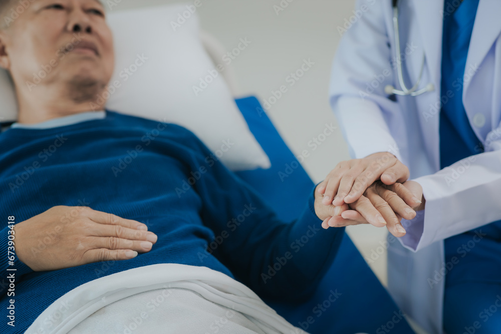 Beautiful Asian female doctor in white top talking with senior patient at bedside in hospital or clinic ward Beautiful Asian female doctor in white top talking with senior patient at bedside in hospital or clinic ward