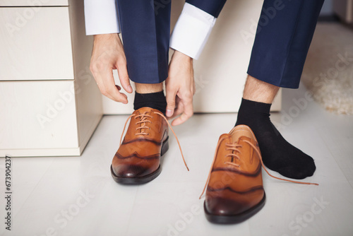 Male businessman puts on stylish shoes. man getting ready for work,groom morning before wedding ceremony. Men Fashion. fastening the laces on the shoes. Man wearing brown leather classic shoes.