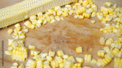 Fresh cooked corn is removed from the stem (cob of corn) using a stenlis knife on a wooden table
 photo