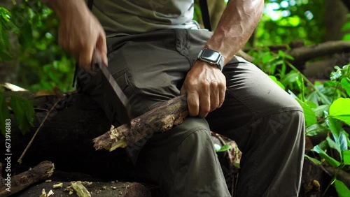 A guy scolds a branch with a knife in a rainforest while sitting in a fallen tree. photo
