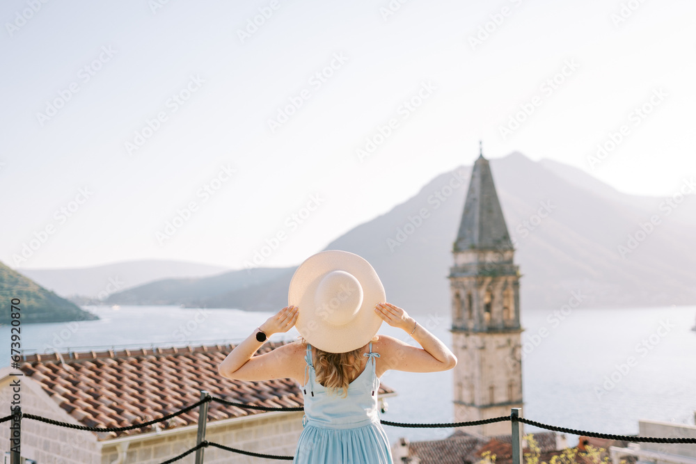 Girl stands on the observation deck near the bell tower, holding her hat with her hands. Perast, Montenegro. Back view