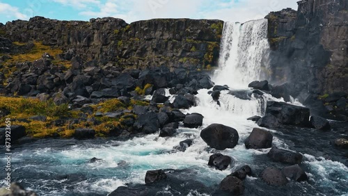 Oxararfoss, spectacular Icelandic waterfall. Course of the Öxará River, in the Þingvellir National Park. Cold water falls on large black boulders of volcanic origin. 4k still shot in slow motion.