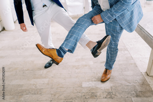 Groom and best man compete by showing their shoes on their outstretched legs. Cropped. Faceless