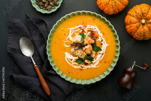 Pumpkin and carrot cream soup with herbs, seasonings and seeds in bowl on black wooden background in rustic style. Thanksgiving traditional autumn pumpkin cream soup. Top view. photo