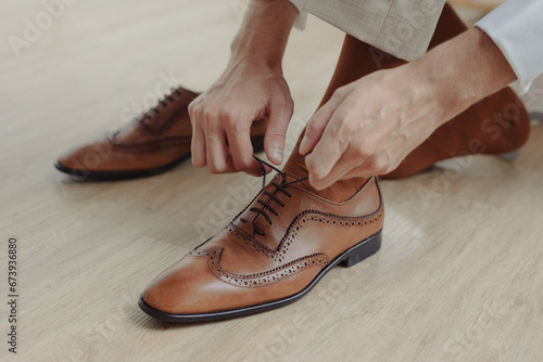 groom binding brown leather shoes on the floor photo