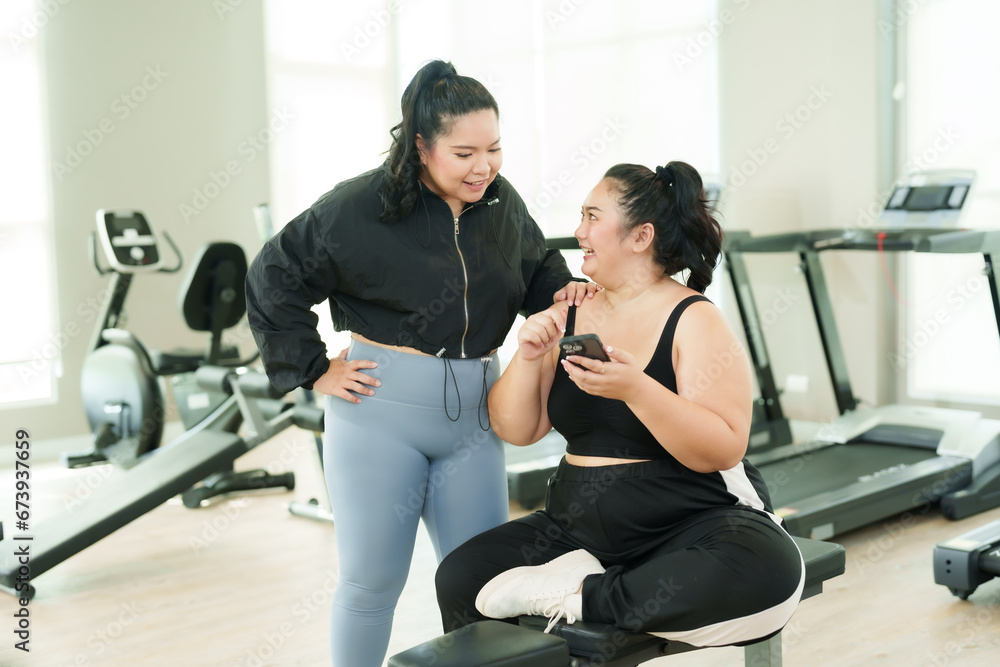 Two overweight asian women look at their smartphones during an exercise break to prepare for weight loss. Young women are using their smartphones to search for a restaurant to eat after exercising.