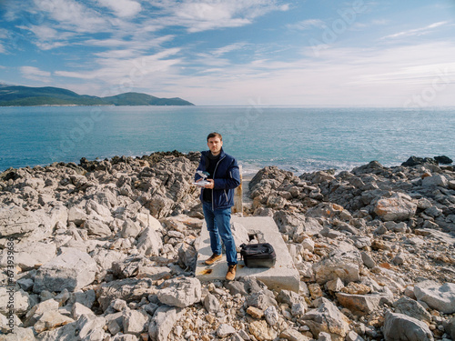 Photographer with a drone in his hands stands on a rocky seashore