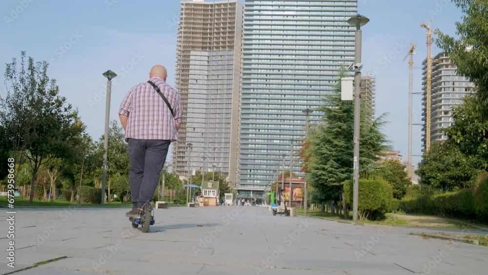 Rear view of plus size man riding e-scooter in the city. Male driving electric scooter outdoors. Electric and ecological transport. Eco-friendly transportation . Sustainable lifestyle concept Rear view of plus size man riding e-scooter in the city. Male driving electric scooter outdoors. Electric and ecological transport. Eco-friendly transportation . Sustainable lifestyle concept