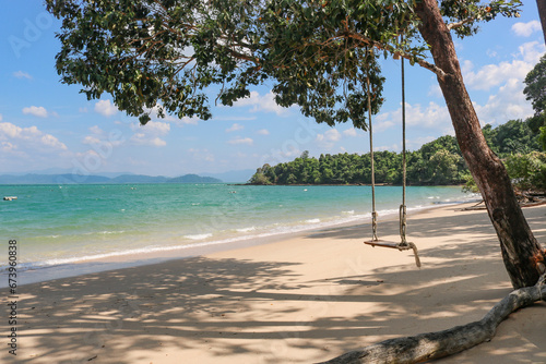 The old rope wooden swing against the backdrop of a beautiful blue sea with clear azure water. Tropical paradise, time for vacation and relaxation.