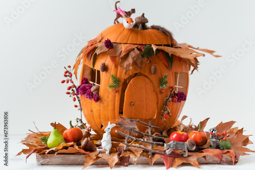 Handmade pumpkin house decorated with fallen leaves, flowers and miniature animals on the white background. Autumn background for Halloween holiday photo