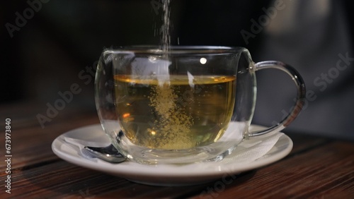 Person adding sugar into green tea in transparent cup at wooden table in housing