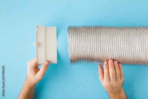 Man hands holding plastic adapter and corrugated aluminium pipe on blue table background. Point of view shot. Assembling new ventilation parts for kitchen cooker hood or air conditioning. Closeup. photo
