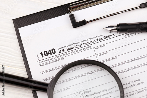 Form 1040 US Individual Income Tax Return on A4 tablet lies on office table with pen and magnifying glass close up