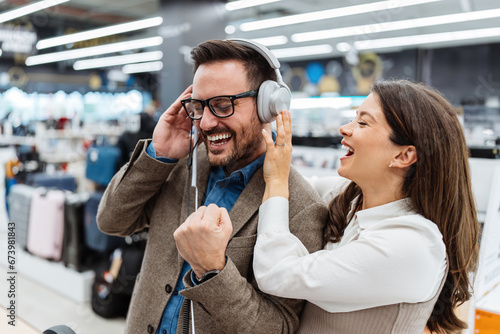 Beautiful and happy middle age couple buying consumer tech products in modern home electronics store. They are choosing high quality hi-fi audio speakers and audiophiles headphones.