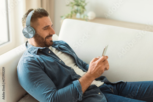 man with smartphone and headphones enjoying music resting at home