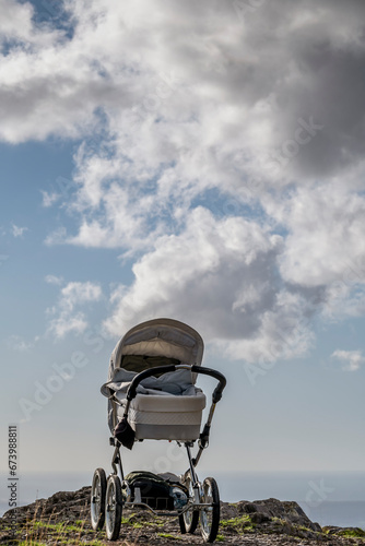 An empty baby stroller is on top of a mountain with the sky with clouds in the background