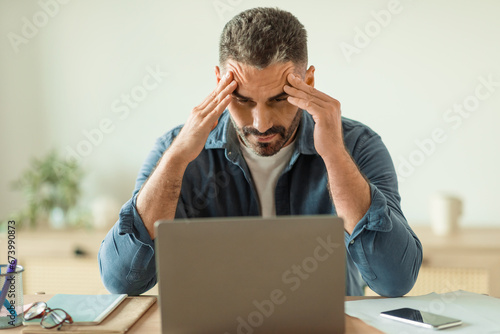 man having stress and headache while looking at laptop indoor