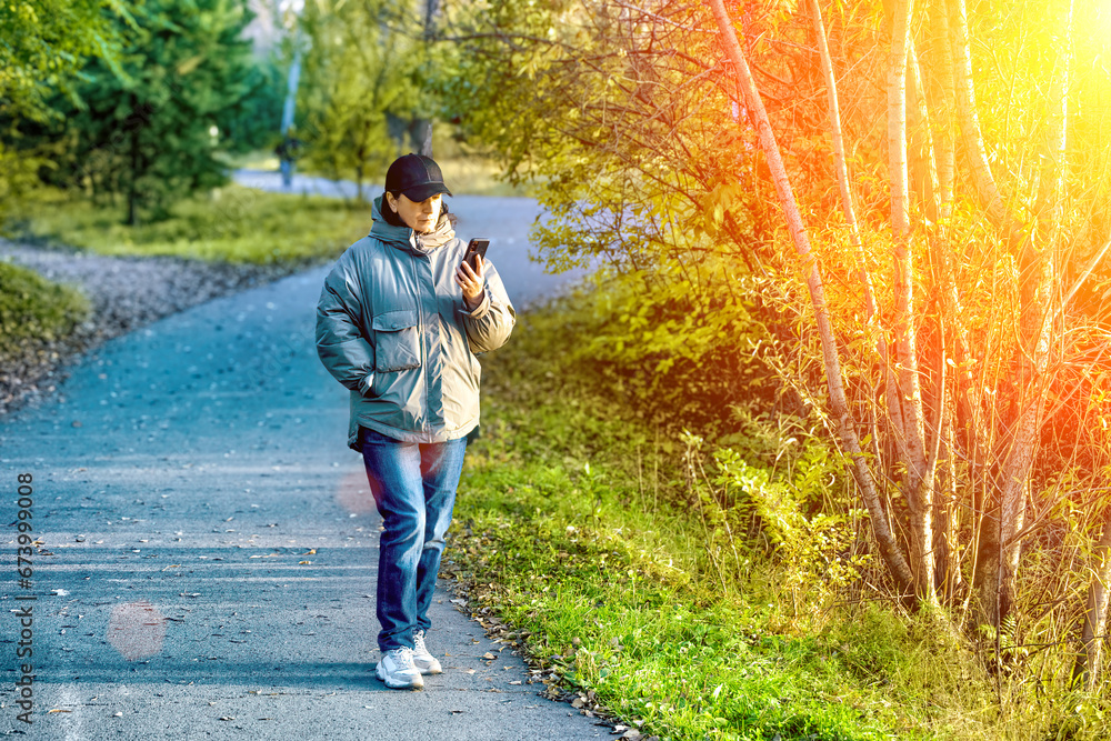 A woman using a smartphone at a tree walking in a park in summer. A woman using a smartphone at a tree walking in a park in summer.