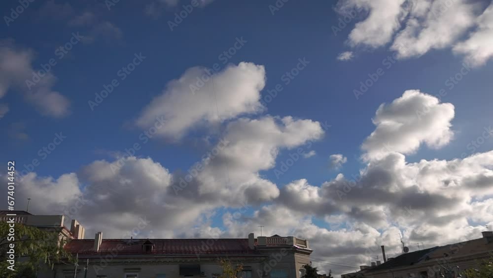 Time lapse video of white clouds moving on a clear blue sky over tree and houses in the city. On the left, the roof of the house is being repaired, workers walk on the roof. Time lapse video of white clouds moving on a clear blue sky over tree and houses in the city. On the left, the roof of the house is being repaired, workers walk on the roof.