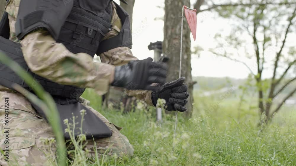 Demining works. War shells lie in the grass on a sunny day. The sapper puts a red mark next to dicovered mine Demining works. War shells lie in the grass on a sunny day. The sapper puts a red mark next to dicovered mine