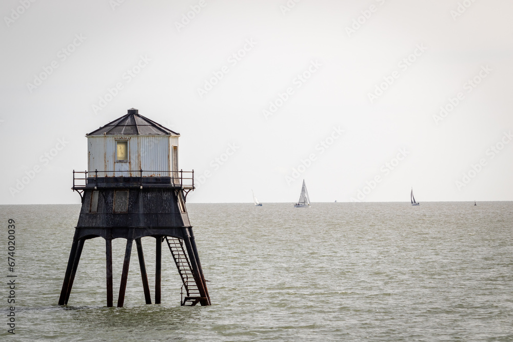 Old lightouse in the sea, Dovercourt low lighthouse, built in 1863 and discontinued in 1917 and restored in 1980 the 8 meter lighthouse is still a iconic sight, with sailing boats sailing past - obrazy, fototapety, plakaty 