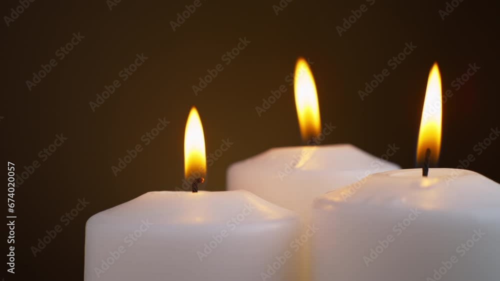 Three white candles are burning on a brown background. taken in close-up. Three white candles are burning on a brown background. taken in close-up.