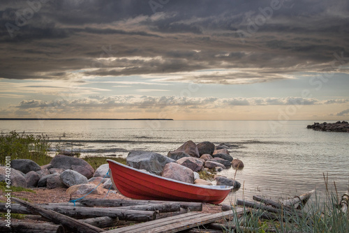 фотографія small boat on a beach, Image shows a small red dingy on a beach next to a wooden boat ramp with a number of smooth large rocks going out to a calm sea, during a summers sunset
