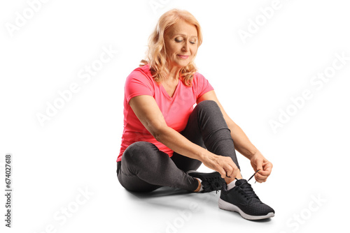 Mature woman in sportswear sitting and tying shoelaces