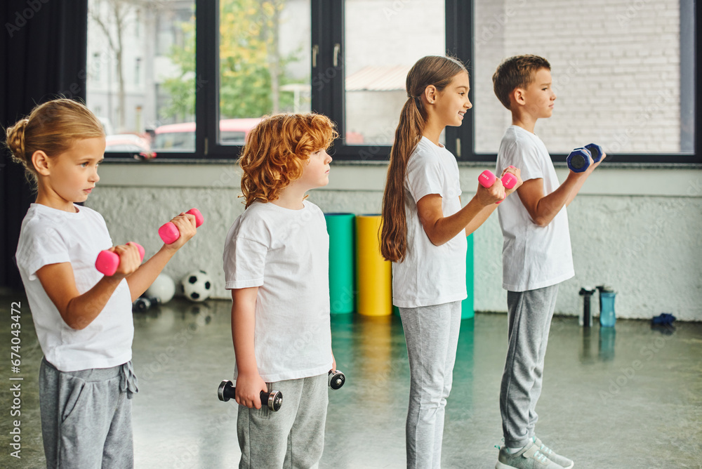 little children posing in profile holding dumbbells with fitness mats and balls on backdrop, sport little children posing in profile holding dumbbells with fitness mats and balls on backdrop, sport