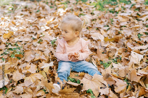 Little girl sits among the fallen leaves in the park and looks away