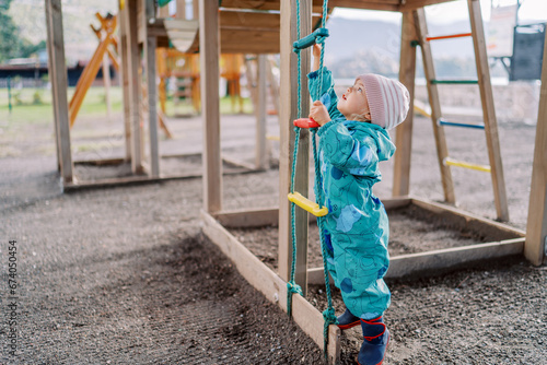 Little girl is trying to reach the top rung of a rope ladder by standing on her tiptoes photo