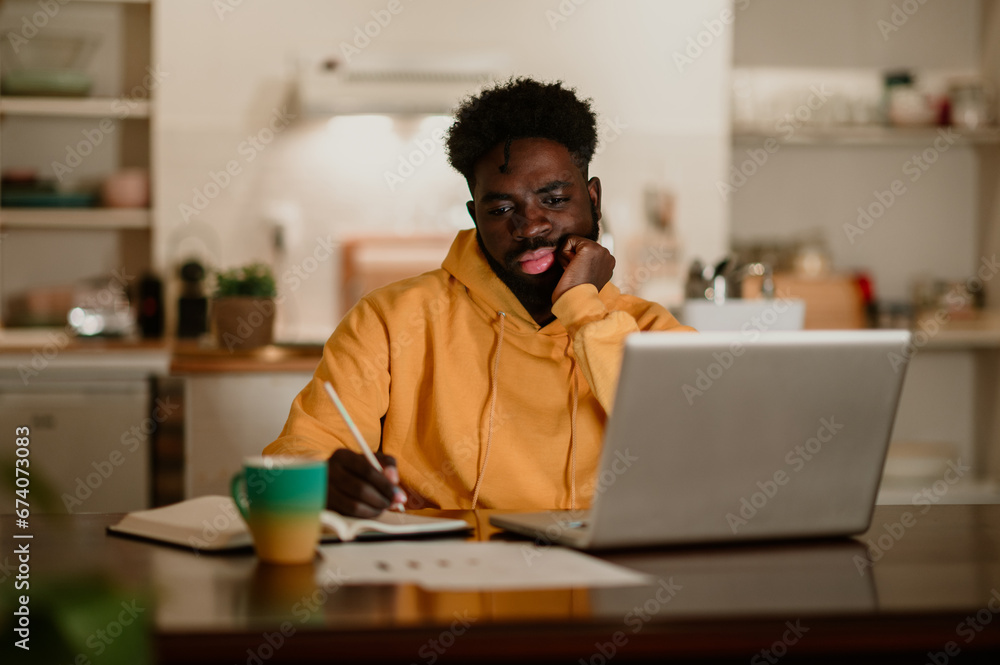 A focused african american student is sitting at home studying late at night. A focused african american student is sitting at home studying late at night.