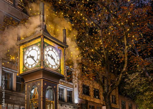 Iconic Gastown Steam Clock illuminated at night on Water Street with fall foliage trees and lights in the background on a beautiful autumn evening, Vancouver, British Columbia, Canada (October 2021).