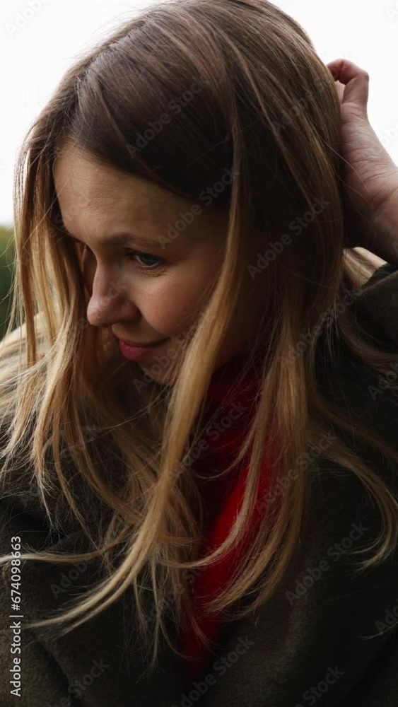 a girl in an autumn coat laughs and looks at the camera. autumn is cloudy. vertical video a girl in an autumn coat laughs and looks at the camera. autumn is cloudy. vertical video