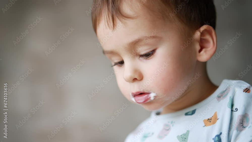 Lovely Caucasian baby boy's face with dairy around his mouth. Close up. Kid eating yogurt at home. Blurred backdrop. Lovely Caucasian baby boy's face with dairy around his mouth. Close up. Kid eating yogurt at home. Blurred backdrop.
