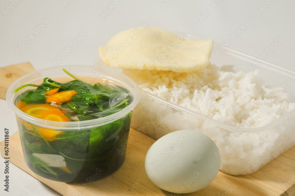 a menu of white rice with clear vegetables of spinach leaves and carrots, side dishes of shrimp crackers and a salted egg on a wooden board isolated on a white background a menu of white rice with clear vegetables of spinach leaves and carrots, side dishes of shrimp crackers and a salted egg on a wooden board isolated on a white background