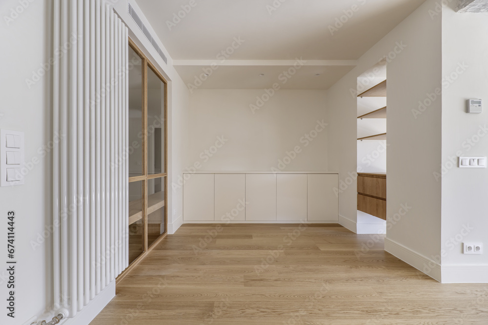 Obraz premium front image of an empty and modern living room with white painted walls and glass and wood partition, large vertical radiator and wooden floors