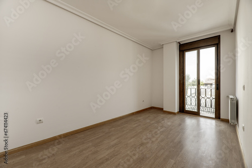 Empty living room or bedroom with white painted walls  double sliding door window with balcony  plaster molding on the ceiling and light wooden and parquet floors