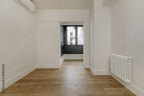 Image of an empty and modern room with plain white painted walls and black glass and metal partition  a large radiator and wooden floors