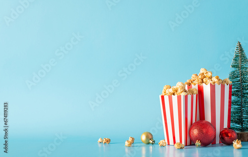 Get cozy with winter flicks: Side view of striped popcorn boxes, ornaments, and a mini Christmas tree against a pastel blue wall for film promotions