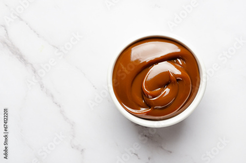 Top view of a bowl full of dulce de leche on white marble background with copy space. 