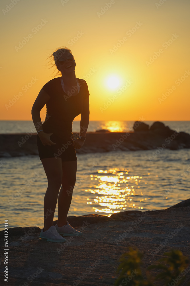 Silhouette of a sporty happy girl at sunset on the sea.
