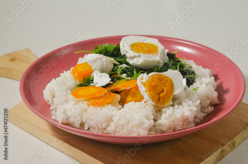 a menu of white rice with clear vegetables of spinach leaves and carrots and a salted egg on a wooden board isolated on a white background